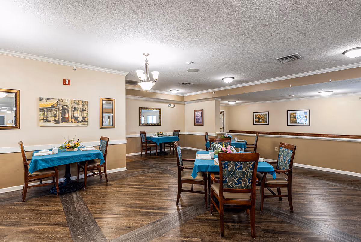 Communal dining room with several tables covered in teal tablecloths, chairs, and framed artwork on the walls.