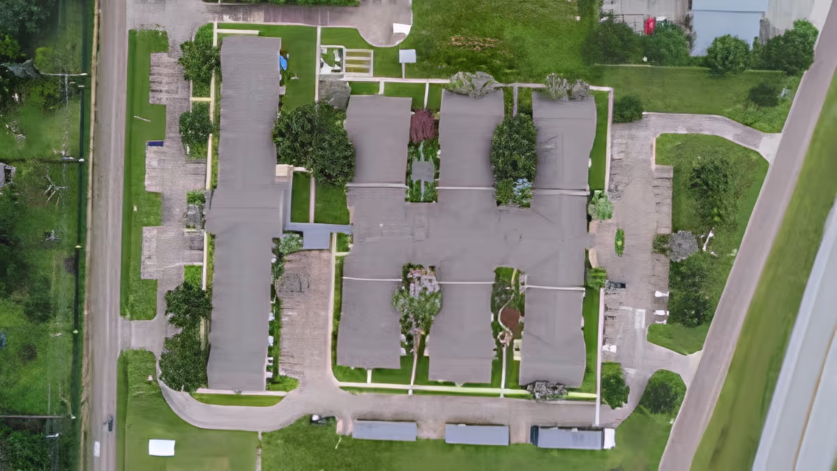 Aerial view of a residential complex with multiple connected buildings, lawns, driveways and surrounding roads.