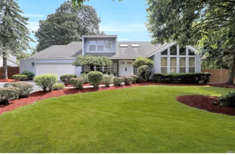 Front exterior of a ranch-style house with a large manicured lawn, shrubs, and an attached garage.