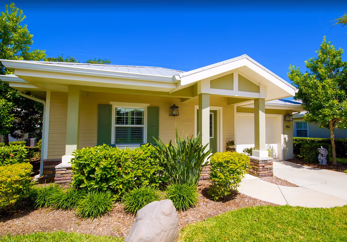 Front exterior of a single-story cottage-style home with a covered porch, garage, and landscaped yard.