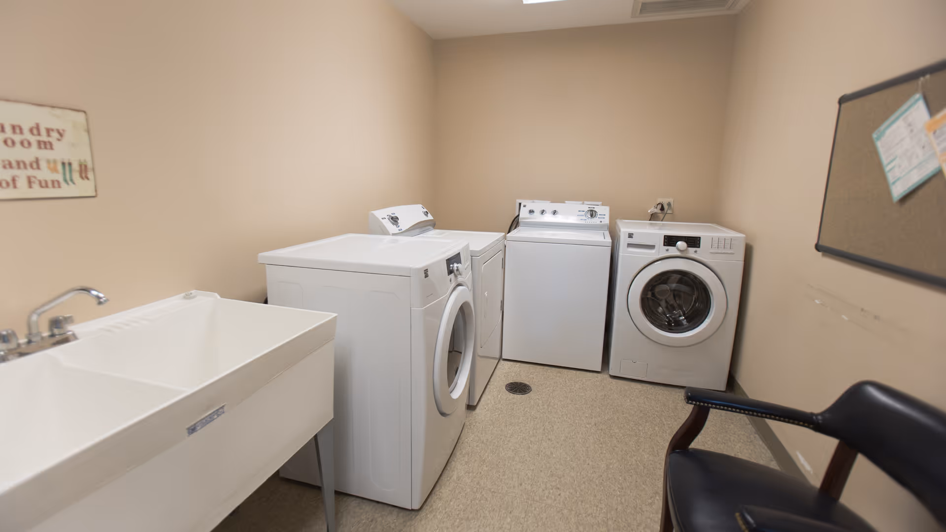 Laundry room with three washers and dryers, a utility sink, a chair, and a bulletin board.