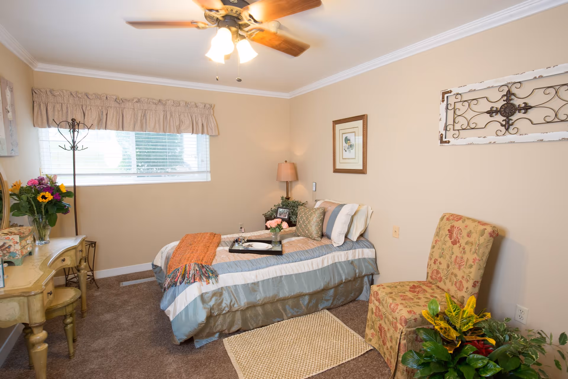 Cozy single bedroom with a bed, floral upholstered chair, vanity table, and ceiling fan.