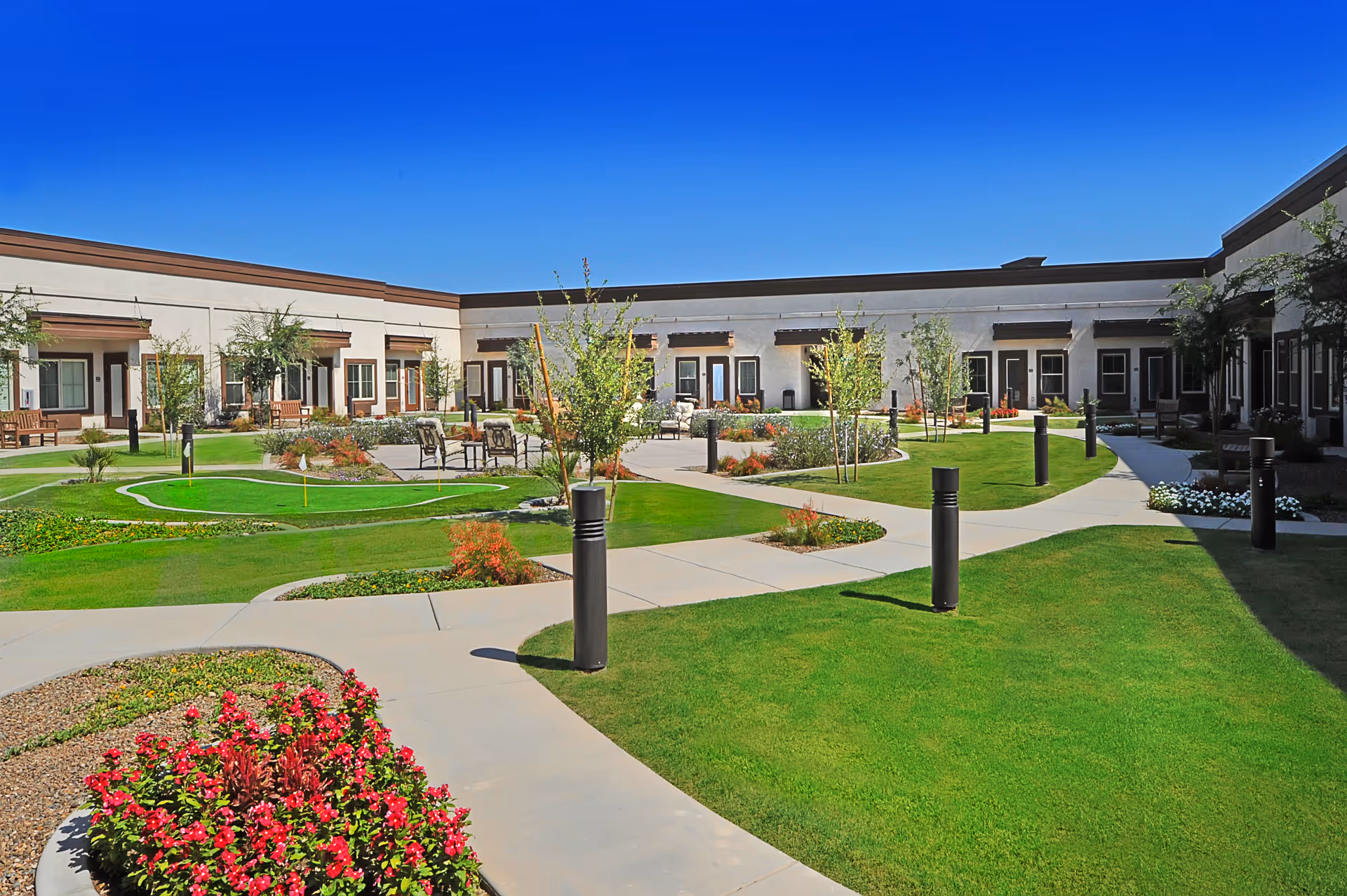 Sunny Sky Ridge courtyard with green lawns, winding paths, trees, benches, and surrounding building wings.