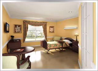 A warmly lit bedroom with yellow walls, a bed, chairs, and a window view.