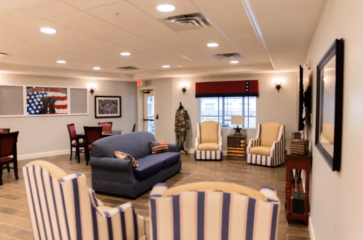 Communal living room with a blue sofa, striped armchairs, dining tables, and patriotic wall decor.