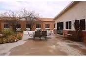 Outdoor courtyard patio with a table and chairs surrounded by single-story senior living facility buildings and planters.