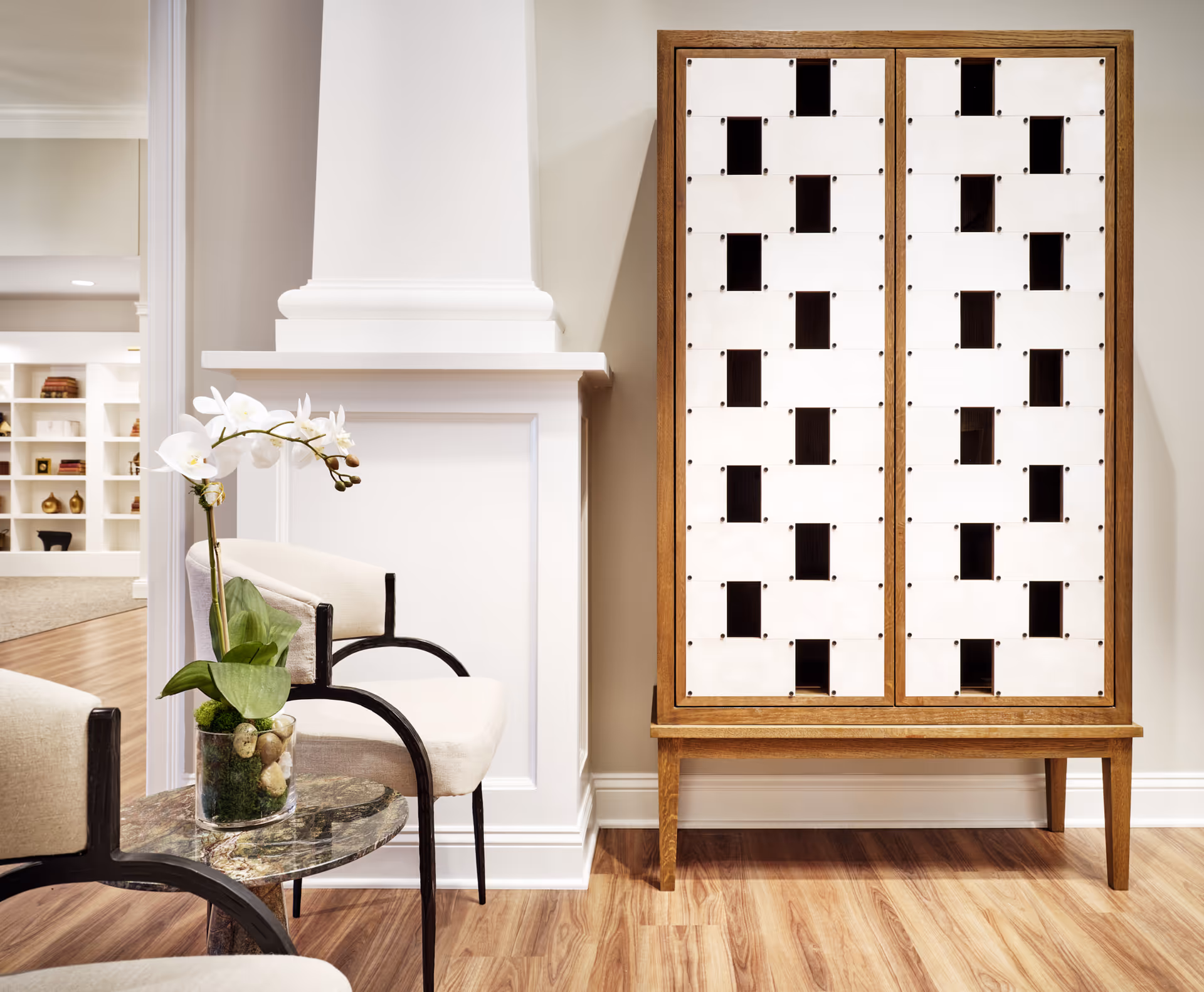 A cozy seating area with modern chairs, a small marble side table holding an orchid, and a tall patterned wooden cabinet against a wall.