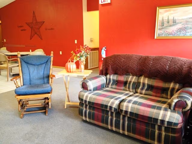 Cozy lounge with plaid sofa, blue rocking chair, fall centerpiece, red walls.
