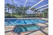 Outdoor swimming pool and hot tub enclosed by a screened structure with a view of palm trees and greenery in the background under a blue sky.
