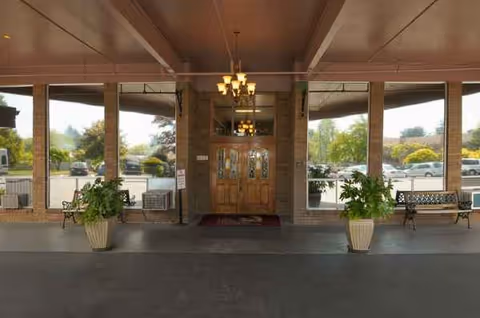Entrance of Life Care Center of McMinnville with double wooden doors, chandeliers, and potted plants.