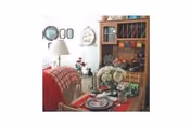 Cozy dining area with a wooden table set for a meal, featuring plates, glasses, and a floral centerpiece. A red plaid blanket is draped over a chair, and a wooden hutch with colorful mugs and decorative items is in the background. A lamp and wall decorations add to the warm ambiance.