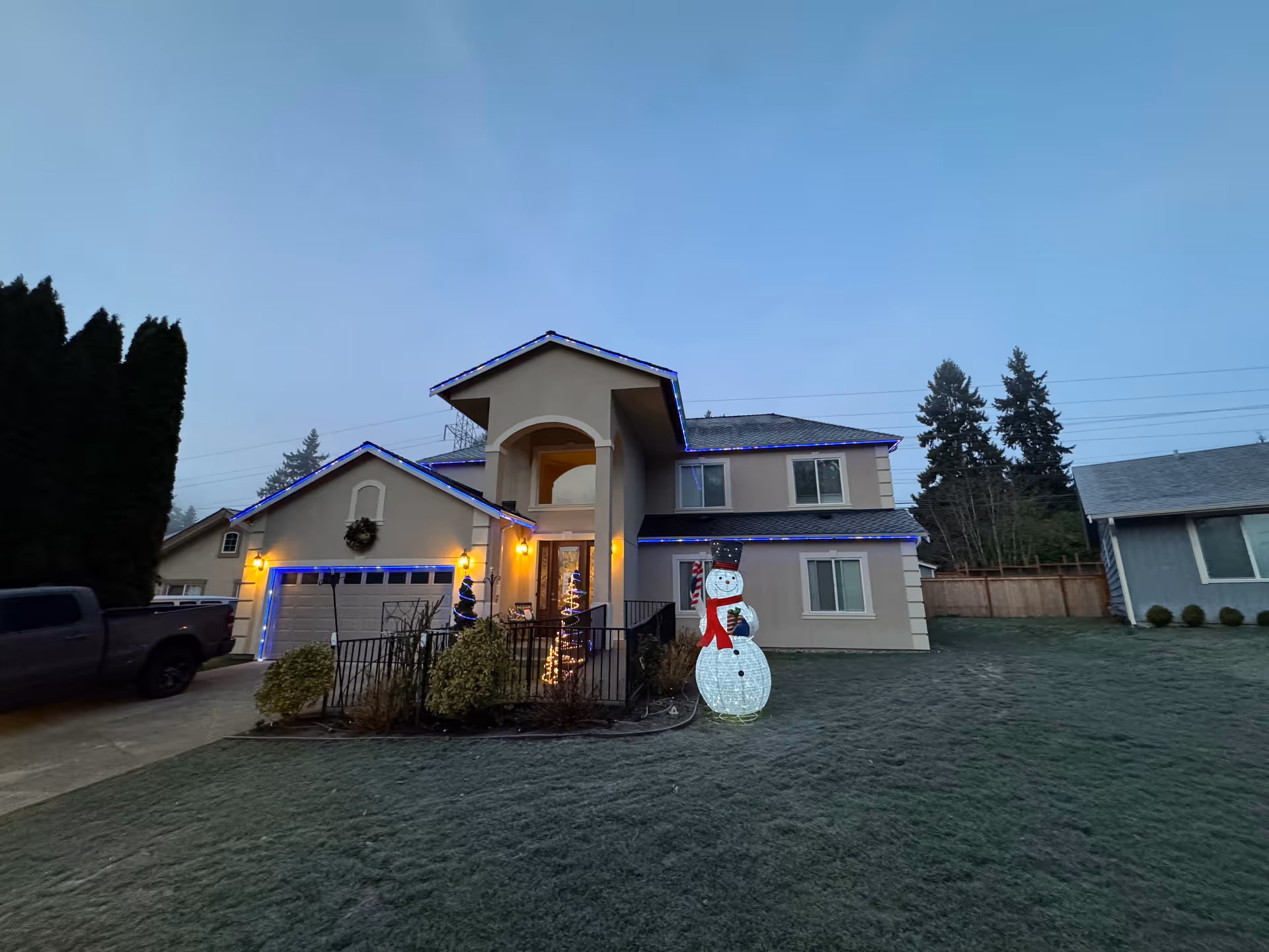 Front exterior of a two-story house decorated with blue holiday lights and an illuminated snowman on the lawn.