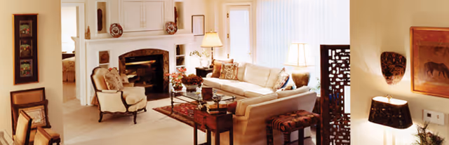 Bright, warmly decorated living room with a fireplace, sofa, armchairs, coffee table and lamps.