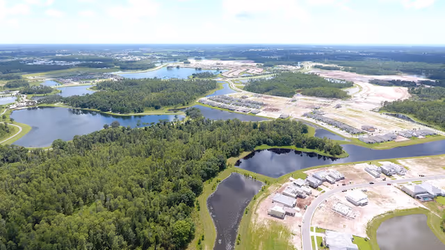 Aerial view of a lakeside residential development under construction surrounded by forests and ponds.