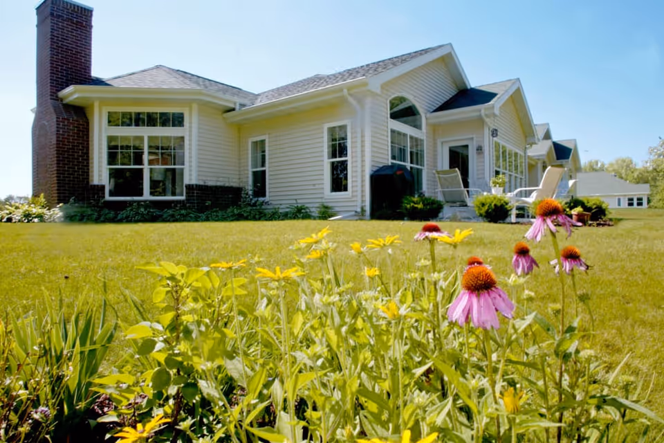 Front exterior of a single-story residential building with a grassy lawn and flowering plants in the foreground.