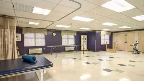 A large, empty rehabilitation room with a treatment table and exercise equipment.