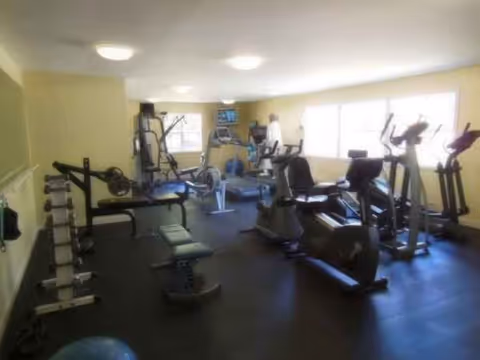 Well-equipped senior fitness center with cardio machines, weights, benches, and bright windows.