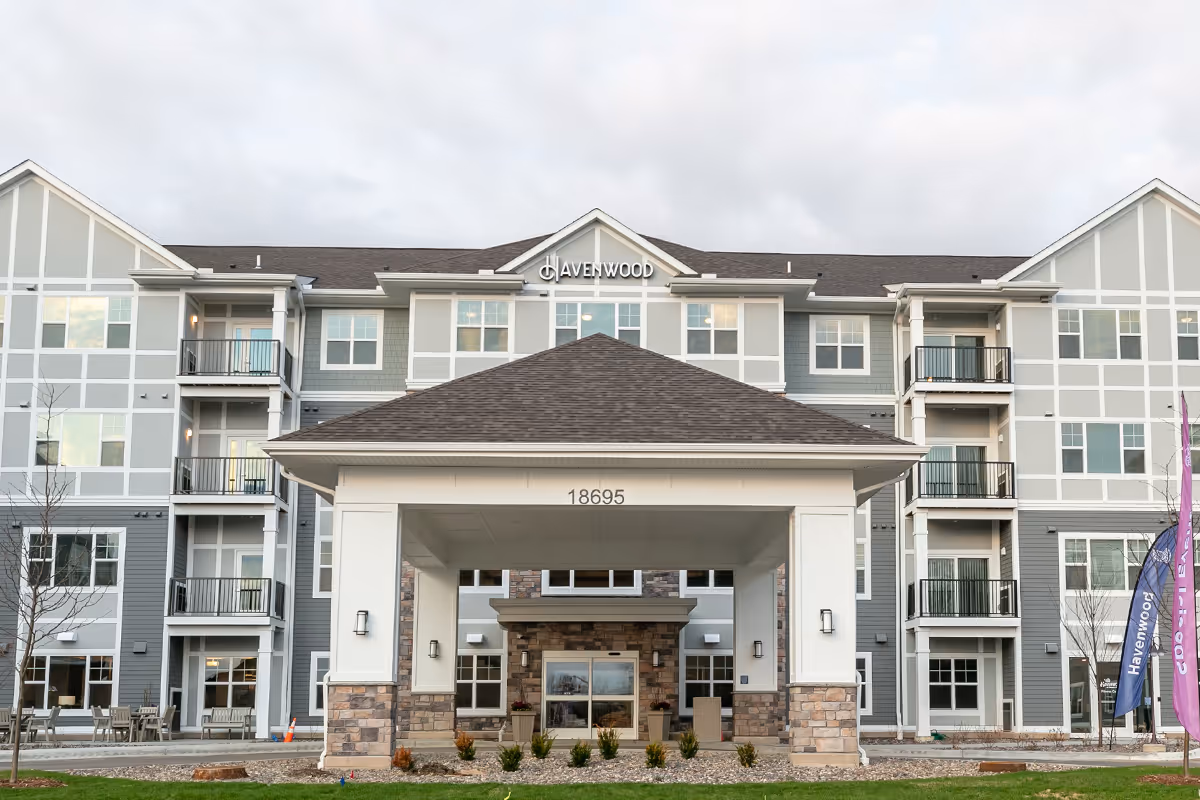 Front entrance of the Havenwood of Maple Grove building showing a covered porte-cochere, balconies, and signage.