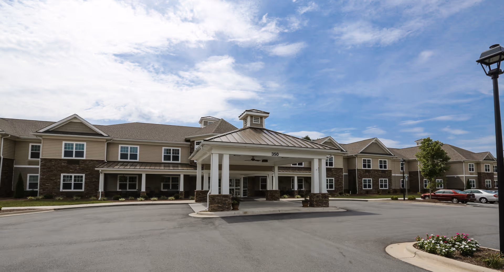 Front exterior of a two-story senior living building with a covered porte-cochere entrance and parking area.