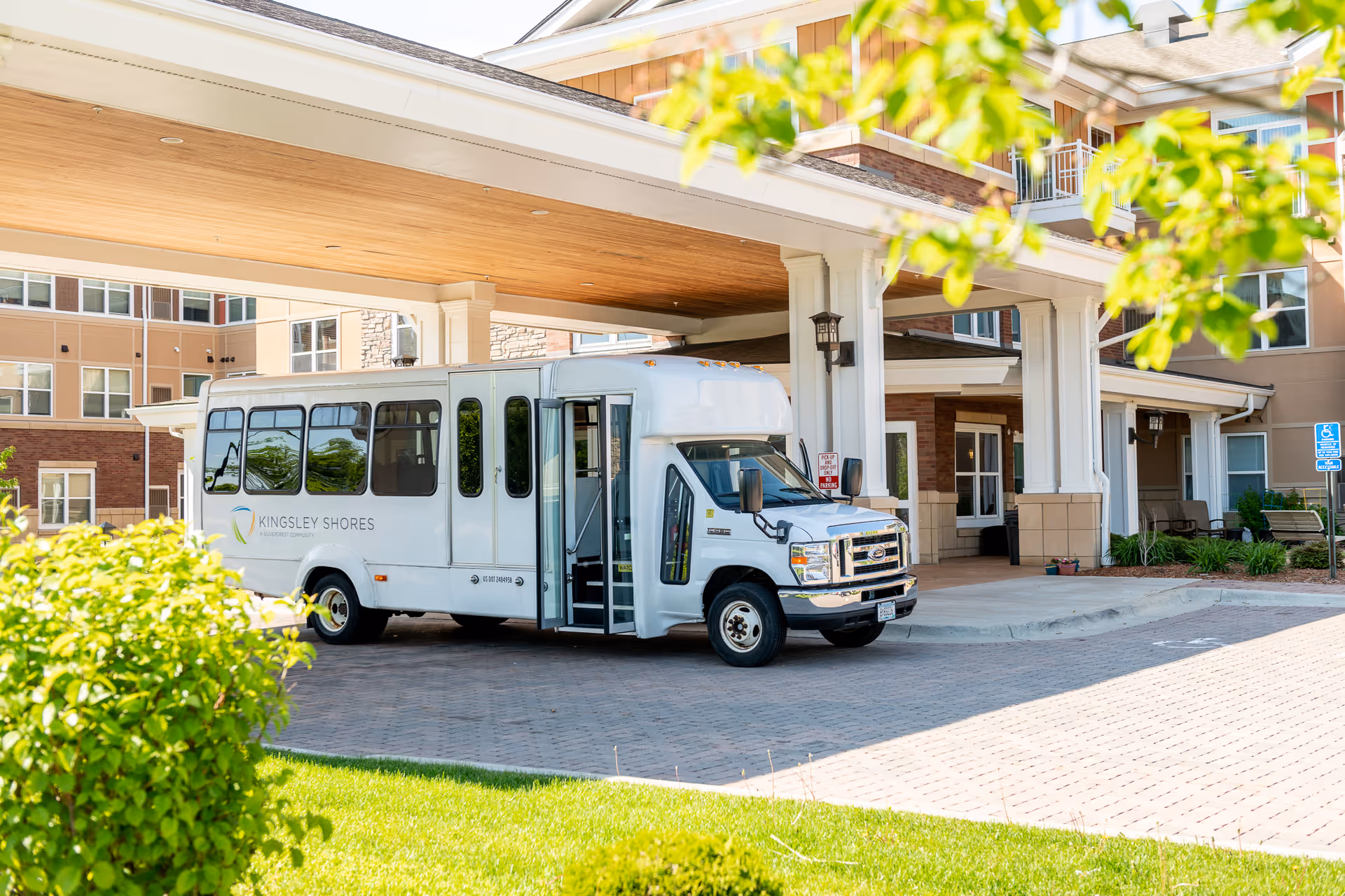 White shuttle bus labeled 'Kingsley Shores' parked under the covered entrance of a senior living building.