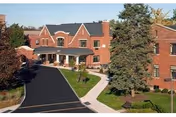 Brick two-story senior living building with a driveway, covered entrance, and landscaped grounds.