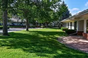 Well-maintained grassy courtyard with trees and single-story residential buildings under a blue sky.
