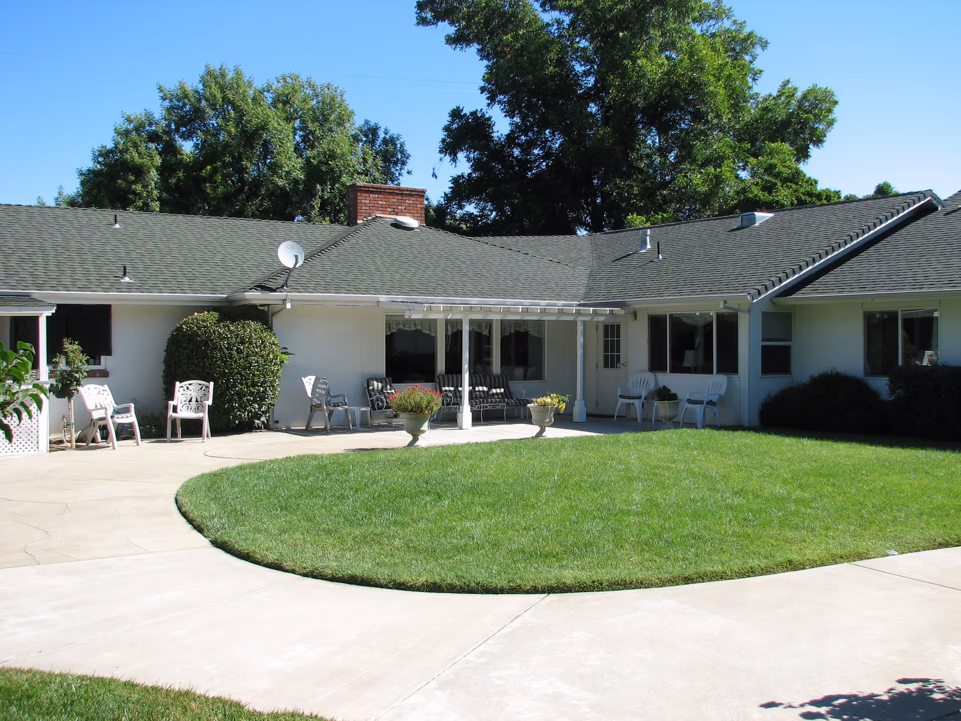 Single-story ranch-style building with a covered patio, outdoor chairs, and a circular grassy courtyard.