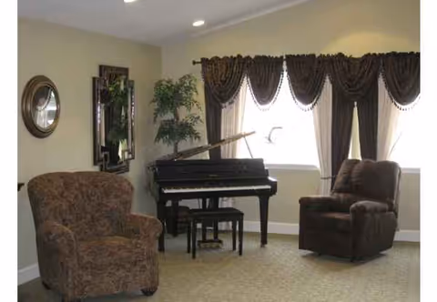 A cozy living room with a grand piano, two armchairs, and draped windows.
