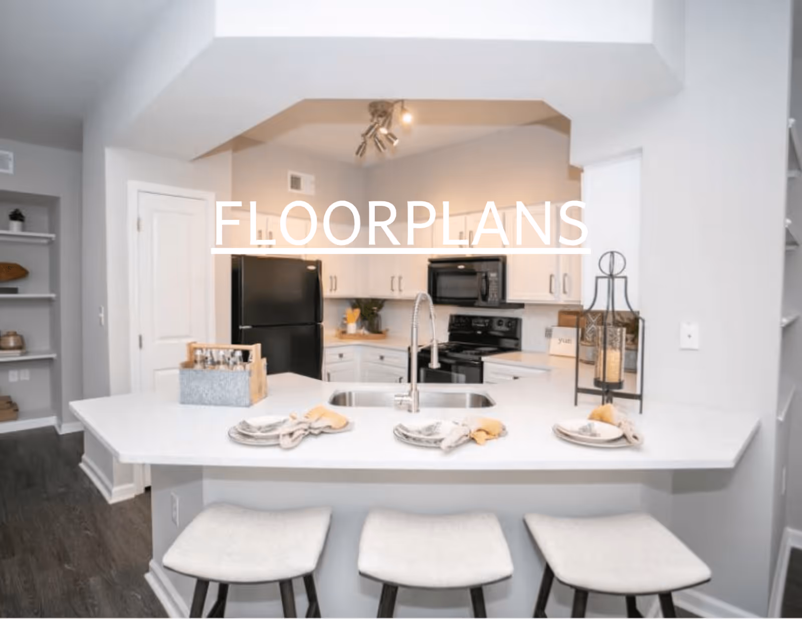 Kitchen with a white island and three bar stools, a sink, and black appliances with the word 'FLOORPLANS' overlaid.