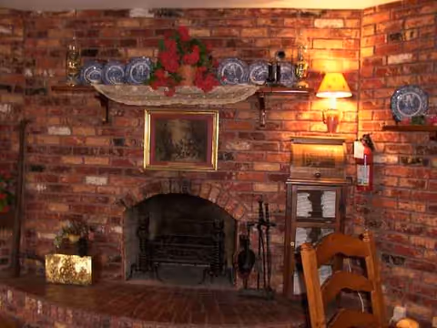 Brick fireplace with mantle, decorative plates, and seating in a cozy living room.