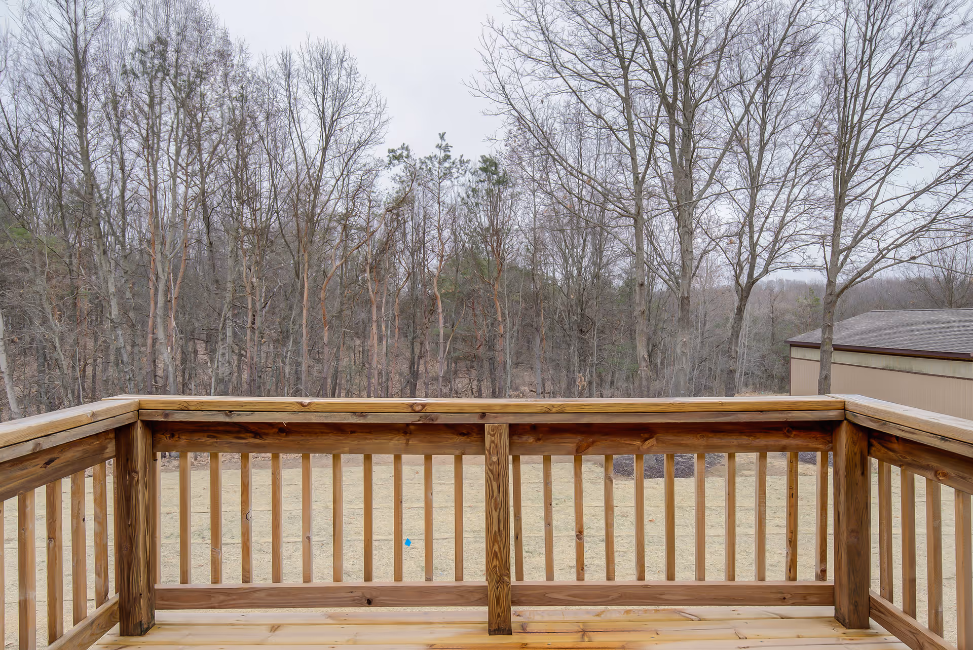 Wooden deck railing overlooking a grassy yard and leafless trees.