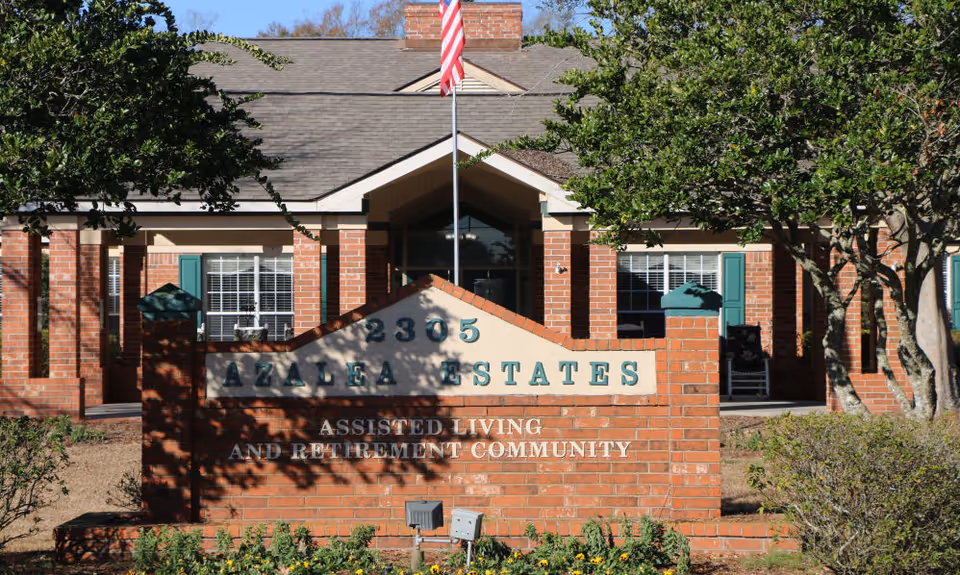 Exterior view of Azalea Estates senior living facility with a sign and American flag.