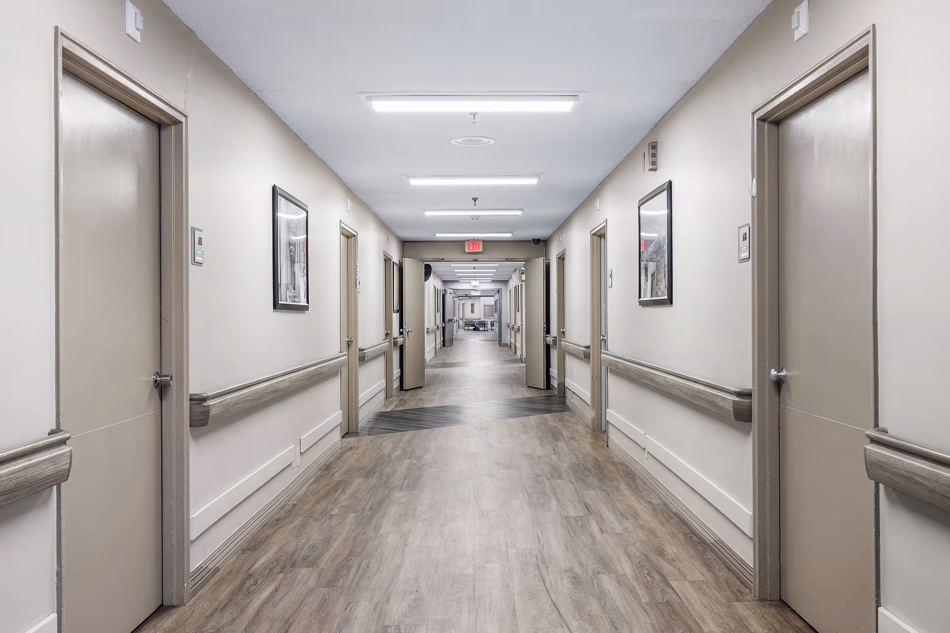 Long, well-lit indoor hallway in a senior living facility with doors and handrails along both sides.