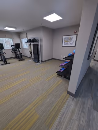 Bright fitness room with exercise bikes, a rack of dumbbells and fitness balls in a senior living facility.