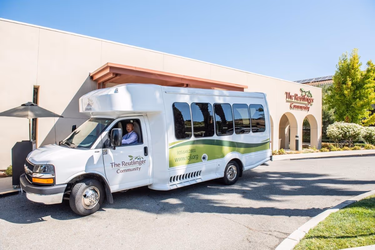 White shuttle bus branded The Reutlinger Community parked in front of a beige building entrance.