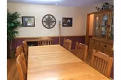 Dining room with a long wooden table and chairs, a china cabinet, wall decorations, and a potted plant.