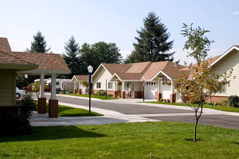 Quiet landscaped street of single-story retirement homes with garages, lawns, and lamp posts.