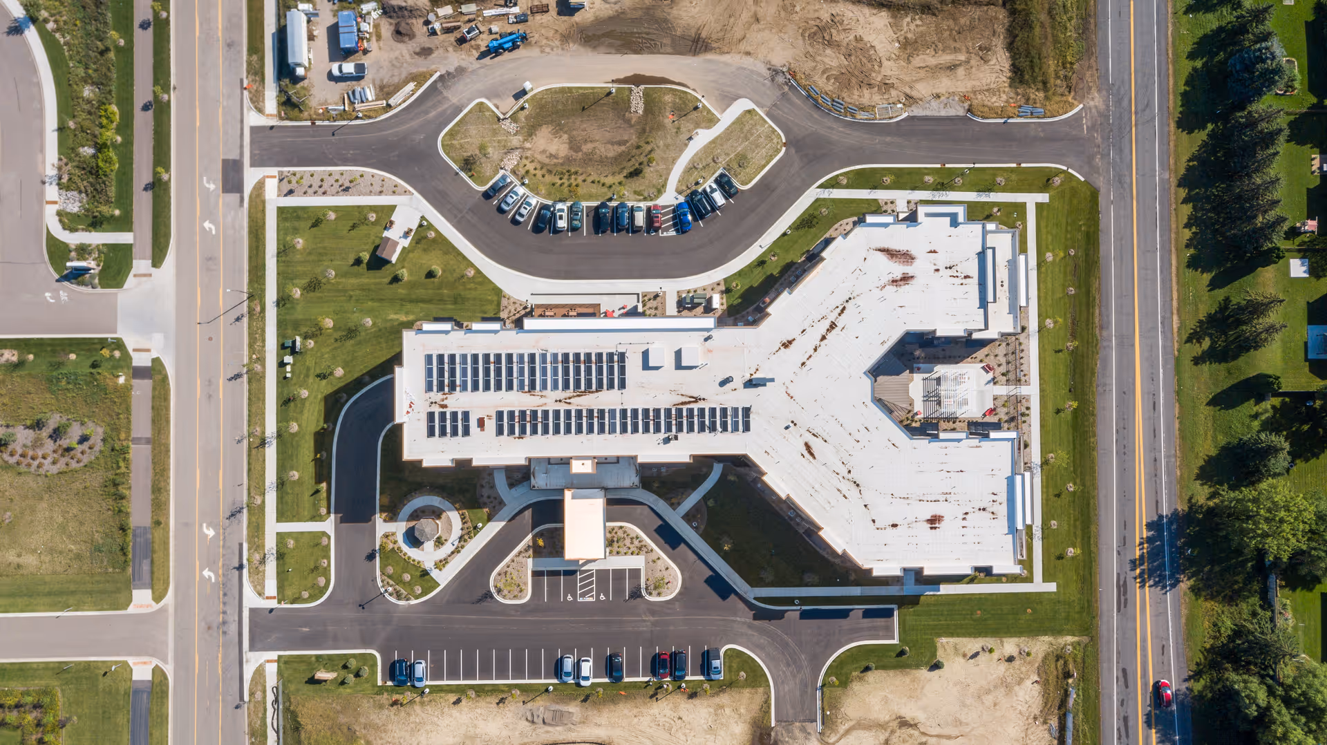 Aerial top-down view of a large senior living building with solar panels on the roof, surrounding parking lots, driveways, and lawns.