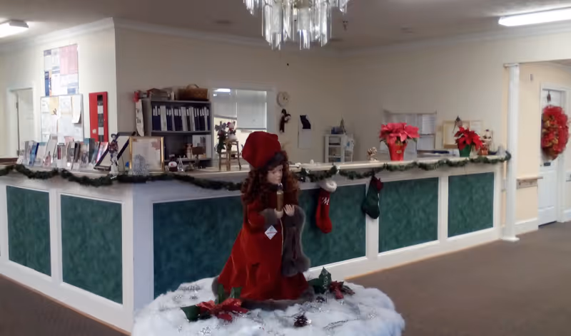 Interior reception area with a decorated front desk and a large red-clothed holiday doll display in front.