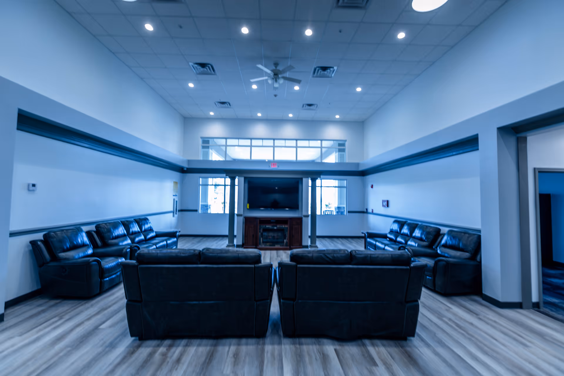 Spacious communal lounge with multiple leather sofas arranged facing a central TV and fireplace under high ceilings and recessed lighting.