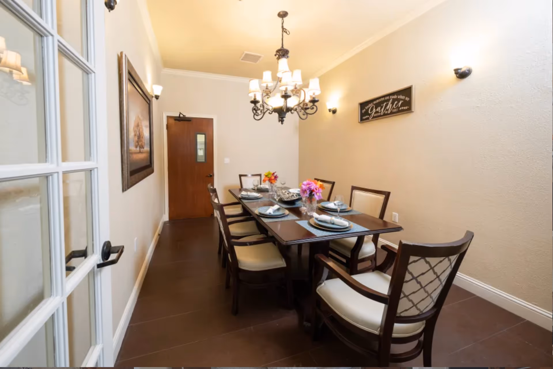 Formal dining room with a long wooden table set for six, upholstered chairs, chandelier, and wall decor.