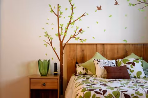 Bedroom with wooden headboard, green floral bedding, nightstand, and tree mural.