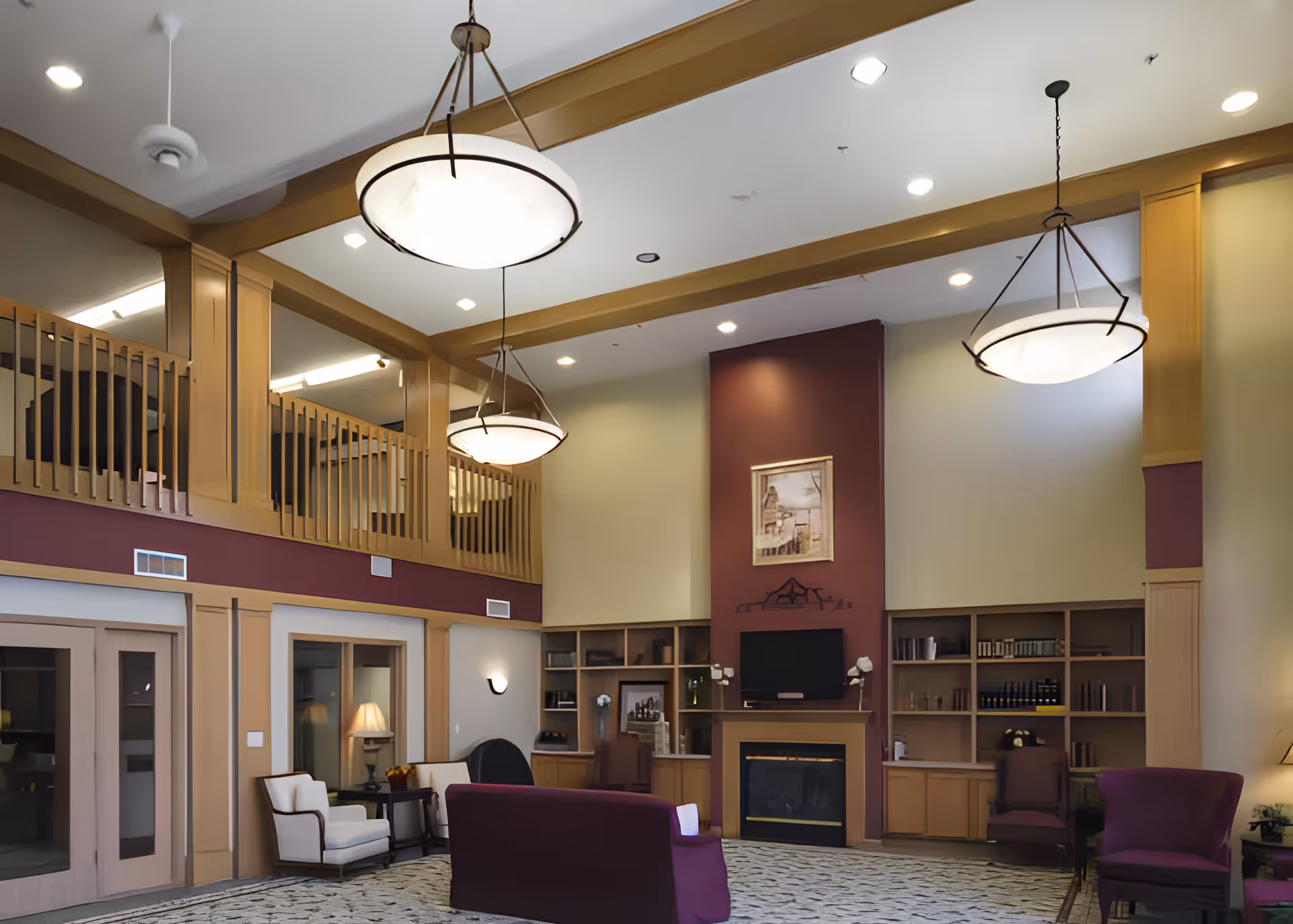 Spacious two-story senior living lounge with seating, fireplace, bookshelves, and hanging light fixtures.
