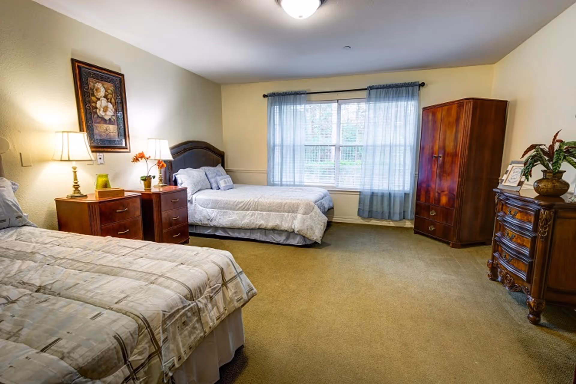 Spacious bedroom with two beds, wooden nightstands, dressers and a large window with blue curtains.