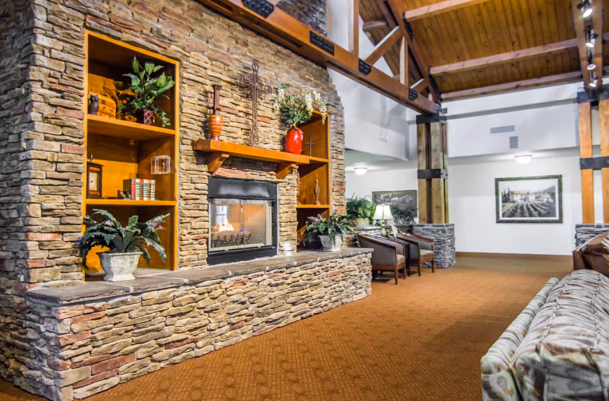 Spacious lounge with a stone fireplace and built-in shelves, seating areas, wood-beamed high ceiling and carpeted floor.