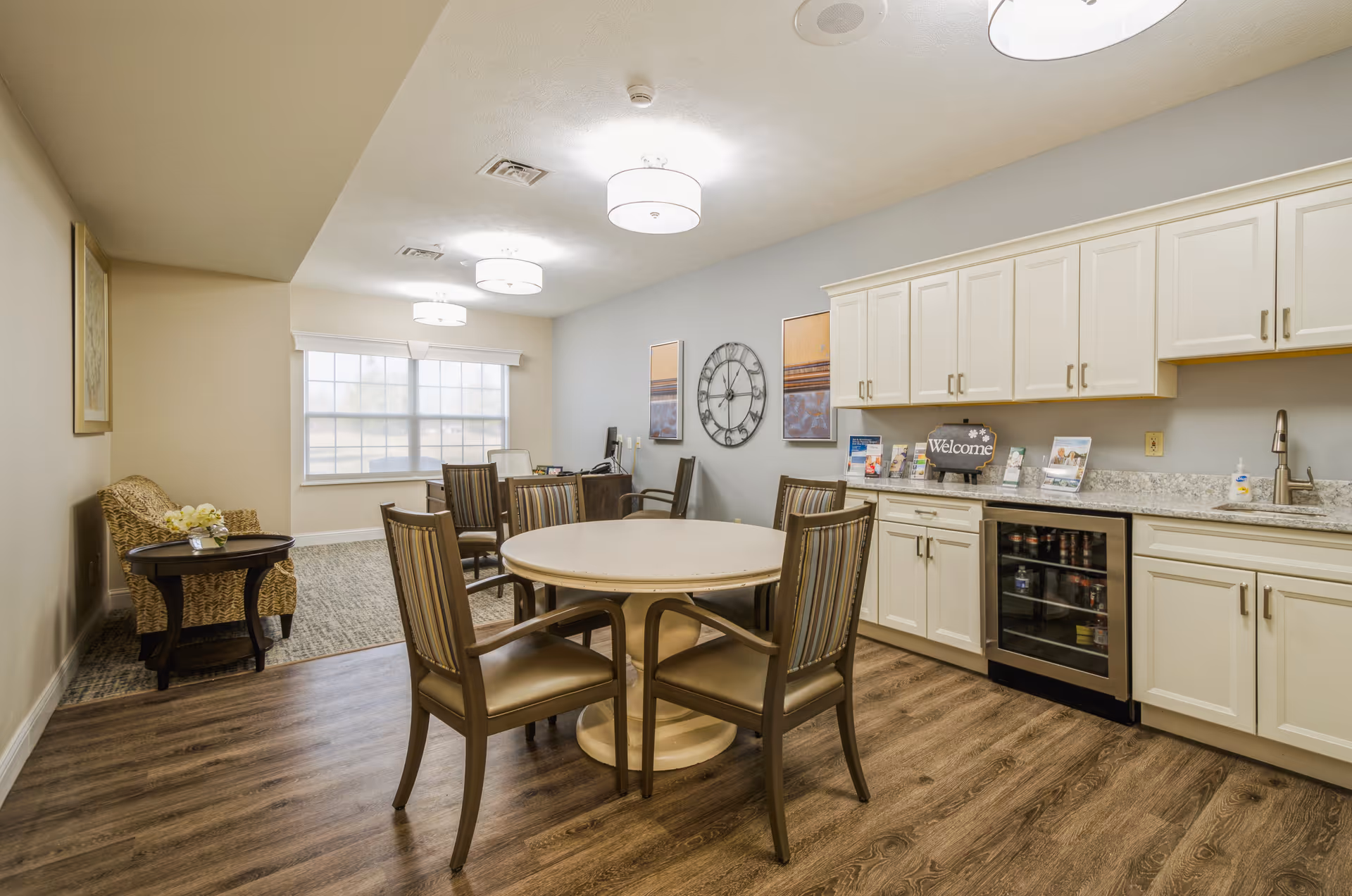 Communal dining and kitchenette area with a round table and chairs, built-in cabinets and a small beverage fridge.