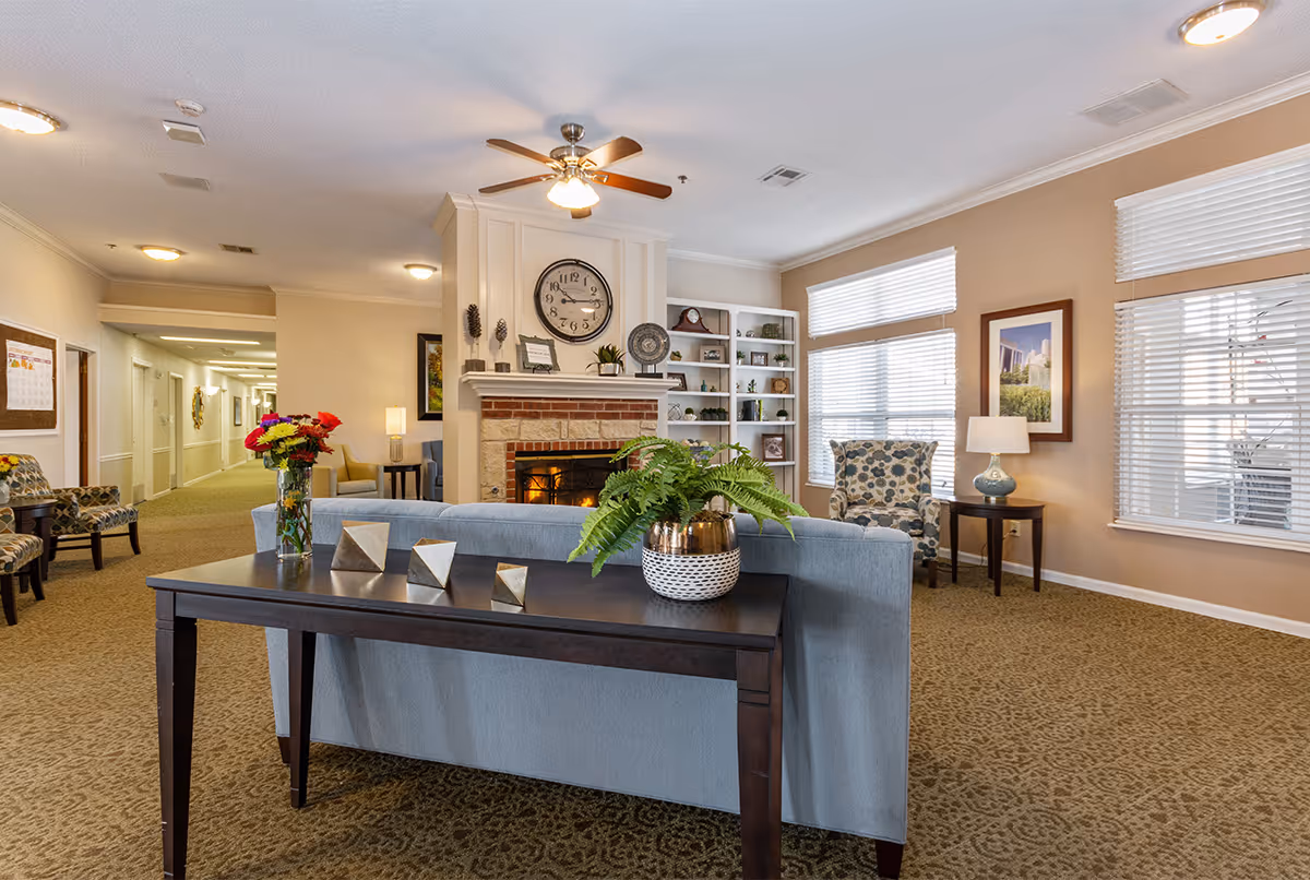 Bright common living room with a fireplace, sofa and console table topped with plants and decor, bookshelves and seating by large windows.