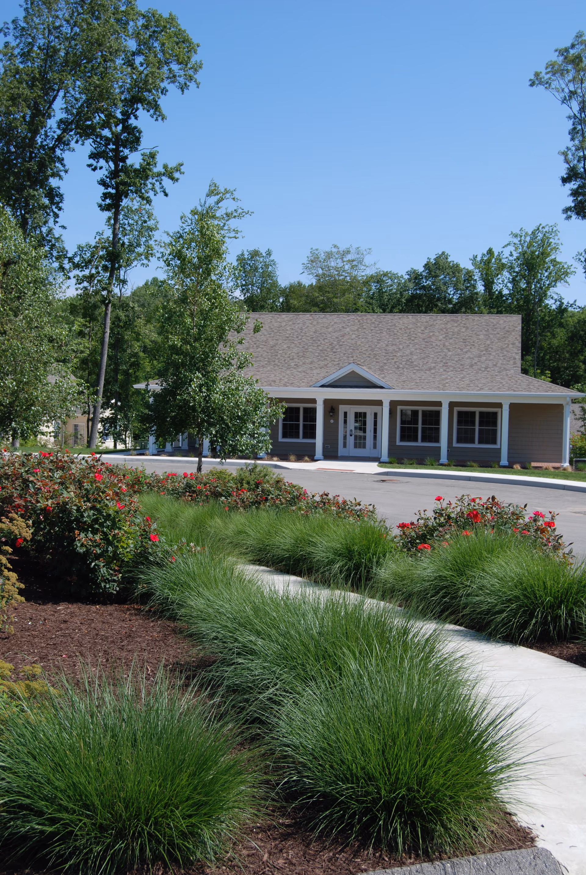Front exterior of a single-story building with a covered porch, surrounded by landscaped shrubs, ornamental grasses, and a walkway.