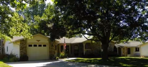 Single-story senior living facility with stone accents, a large shade tree, and front entrance.