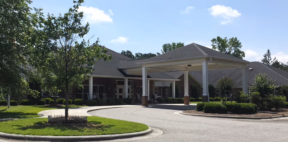 Front entrance of a single-story senior living facility with a covered porte-cochère, driveway, and landscaped grounds.